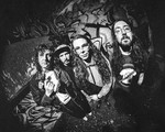 A black and white photo shows the group Tall Mary standing in front of a graffitti wall, each staring into the camera which has a warped vignette effect.