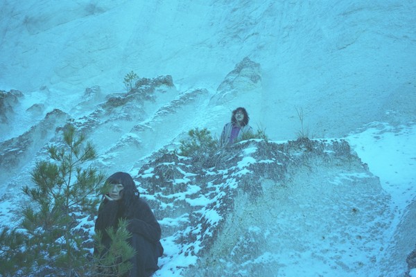 A colour photo shows two members of TANGINGUGUN standing spread out on a snowy mountain landscape. 
