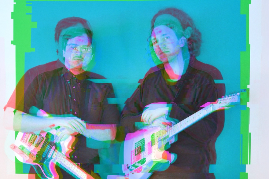 A colour photo with a distorted red and blue 3D type effect shows two members of the band Temps standing side by side wearing all black and both holding white guitars.