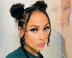 A double exposure photo shows a artist Tinywiings with a close-up on their face, with a faded copy of their face above on the the top right. Their hair is in two tight buns on the top of their head, with two braids hanging down each side. 