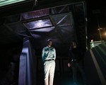 A colour photo shows duo WANTS standing outside at night under a bridge-like structure. Purple light shines from the grate above them. 