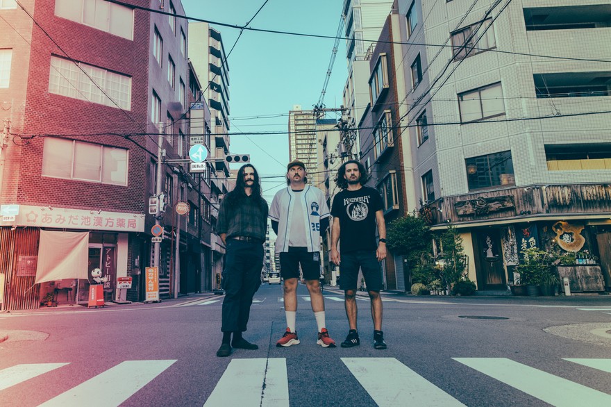A colour photo featuring three members of Weep Wave, posed standing in a Japanese intersection in an urban setting. 