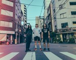 A colour photo featuring three members of Weep Wave, posed standing in a Japanese intersection in an urban setting. 