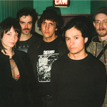 A colour photo of five-piece Witch Victim standing in a green hallway, each facing the camera. Exit sign is above them.