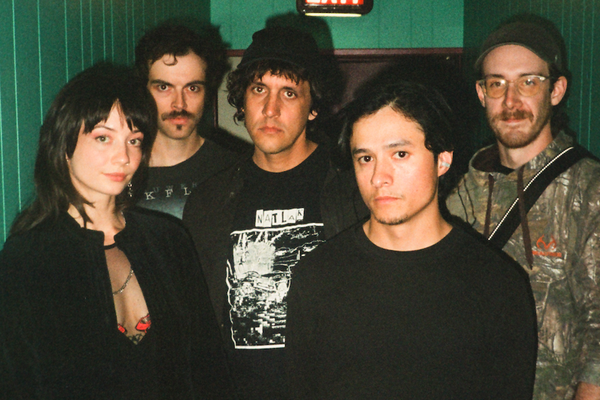 A colour photo of five-piece Witch Victim standing in a green hallway, each facing the camera. Exit sign is above them.