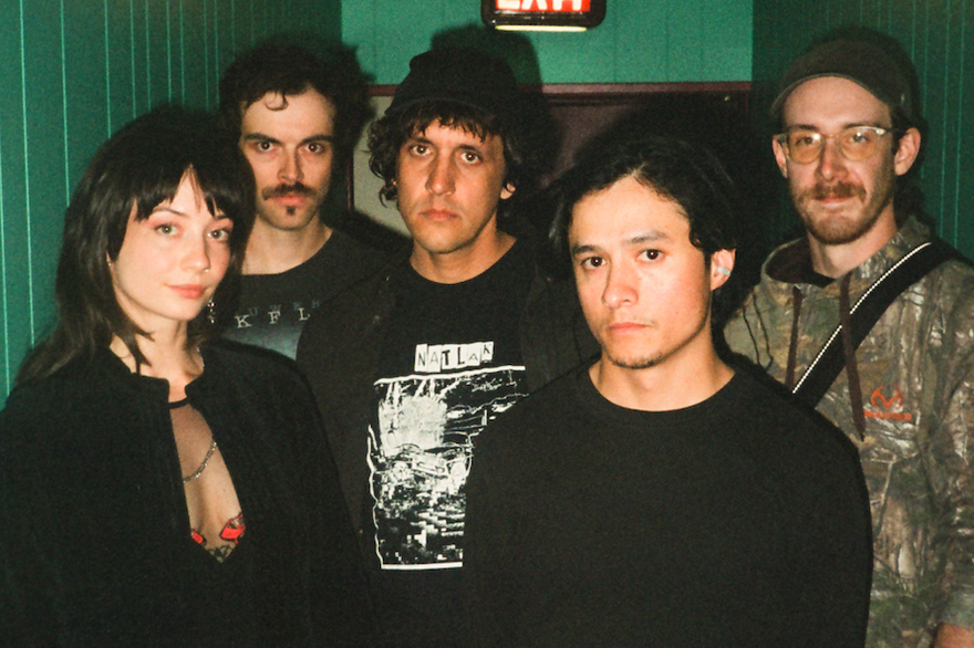 A colour photo of five-piece Witch Victim standing in a green hallway, each facing the camera. Exit sign is above them.