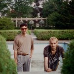 A colour photo of duo World News posed outdoors with an empty pool and hedge bushes in the background. 