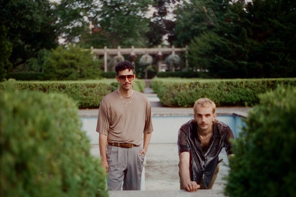 A colour photo of duo World News posed outdoors with an empty pool and hedge bushes in the background. 