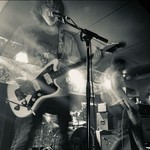A black and white photo of four-piece Yarbo performing in a dimly lit venue.