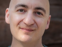 Portrait of comedian Josh Dullard smiling toward the camera in a green sweater.